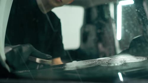 A close-up of a car wash worker using a brush and car chemicals to clean the dashboard of a car