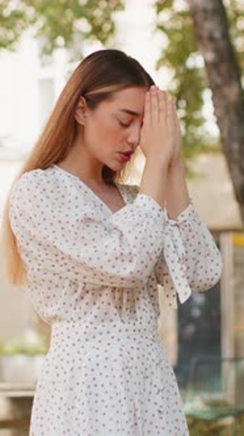 Pensive Woman Holding Hands in Prayerful Gesture Outdoors