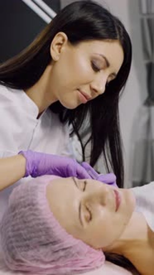 A cosmetologist makes injections for a woman in a beauty center.