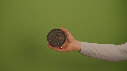 A Hand Gracefully Holding a Clock Set Against a Fresh and Vibrant Green Background