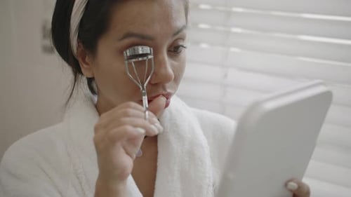 Woman Using Eyelash Curler in Bathroom