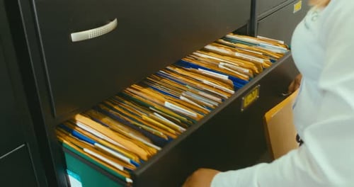 Woman opening a black drawer full of files and folders and filing some documents.