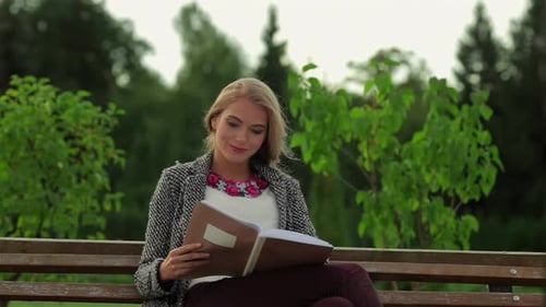 Charming Girl Student Immersed in Reading on a Sunlit Park Bench
