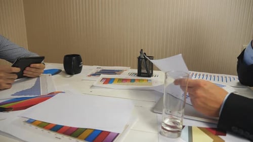 Dos empresarios examinan los informes financieros en un gráfico y una tableta sentados a la mesa