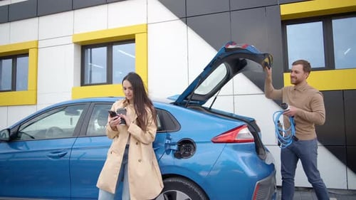 Man takes out the charger plug from the trunk of the electric car before driving around city center