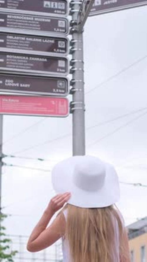 Woman in Hat Looks at City Destination Sign