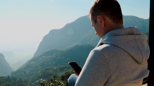 Travel Blogger Sitting with Mobile Phone in Beautiful Mountain Valley