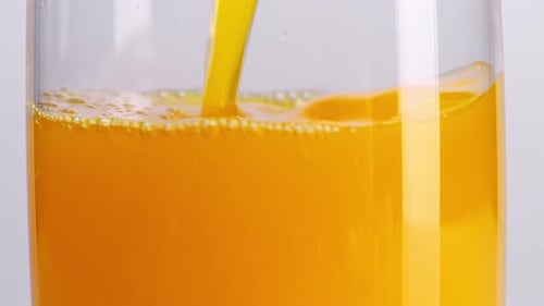 Nahaufnahme von Orangensaft, der in ein Glas auf hellweißem Bildschirmhintergrund gegossen wird