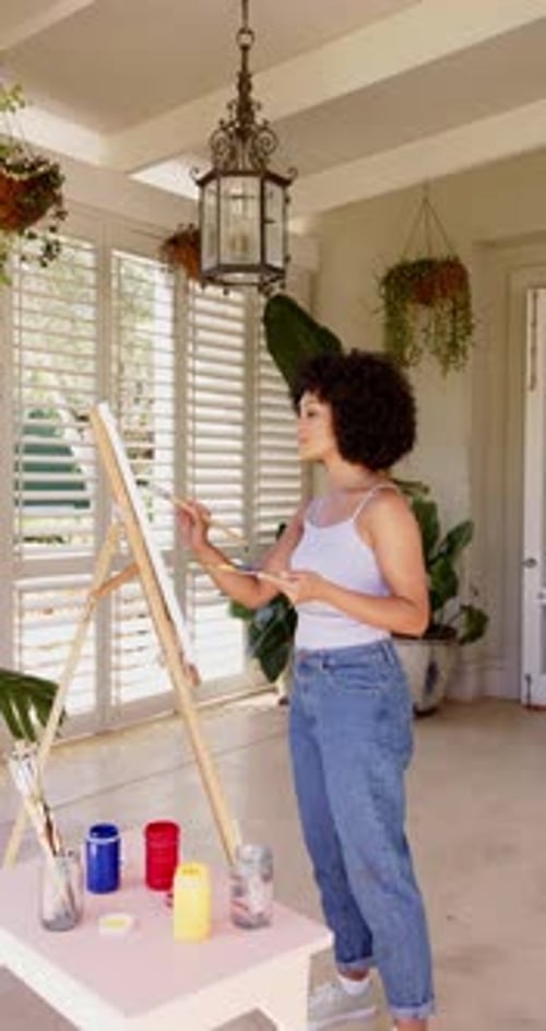 Vidéo verticale : peinture sur toile, femme en tenue décontractée créant de l'art dans une pièce lumineuse