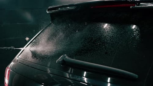 close-up A male car wash employee applies car wash detergent to a black luxury car using spray gun