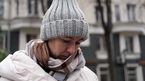Portrait of Mature Woman in Wool Hat Standing on the Urban Street with Mobile Phone in Hand
