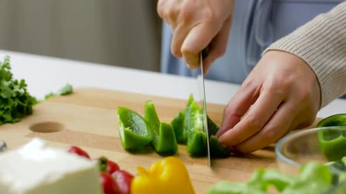 Hands slicing green pepper on cutting board