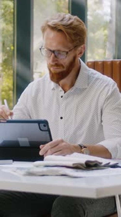 Red-Haired Man Working on Tablet at Desk