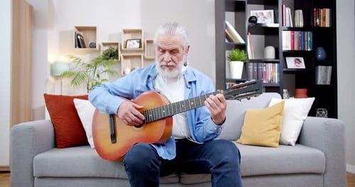Senior Man Plays Guitar on Couch at Home