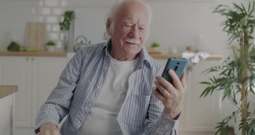 Senior Man Video Chats on Phone in Kitchen