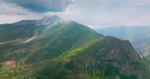 High mountains overgrown with green pine trees under the grey skies.