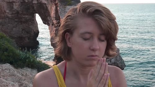 Woman Meditating Peacefully by Ocean on Rocky Coast