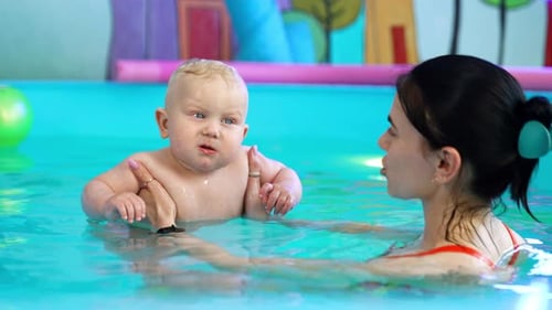 Brunette woman is holding a lovely little baby boy in the swimming pool.