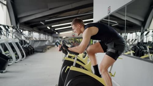 Man exercising on gym bike, wearing shorts, working thighs