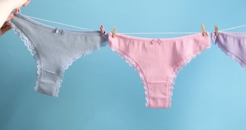 Woman hanging beautiful panties on clothes line against light blue background, closeup