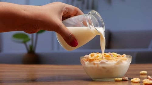 A hand pouring milk into a bowl of cereal