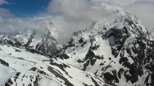 Air flight through mountain clouds over beautiful snow-capped peaks of mountains and glaciers.