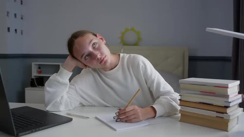 Teenage Girl Daydreaming While Doing Homework at Her Desk