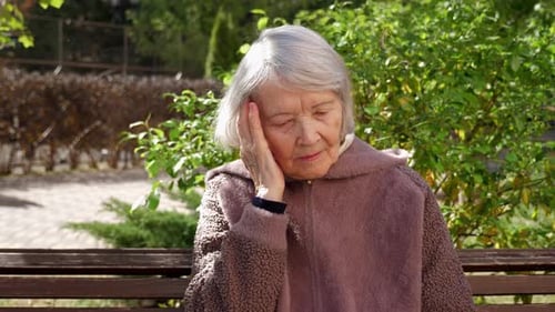 A Grandmother with Gray Hair and a Wrinkled Face in a Park on a Bench