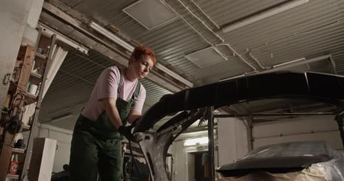Female Technician Sanding Bumper in Garage