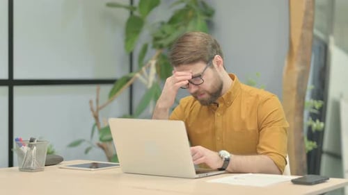 Bearded Man Works at Desk, Rubs Head