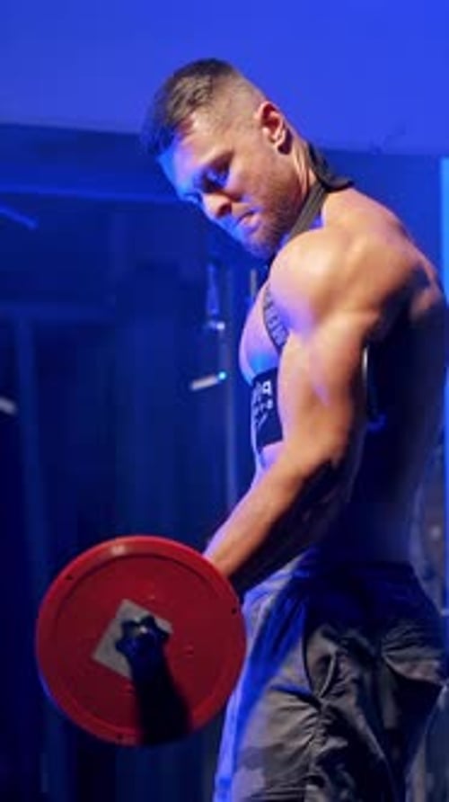 Muscular Man Doing Bicep Curls in Dark Gym
