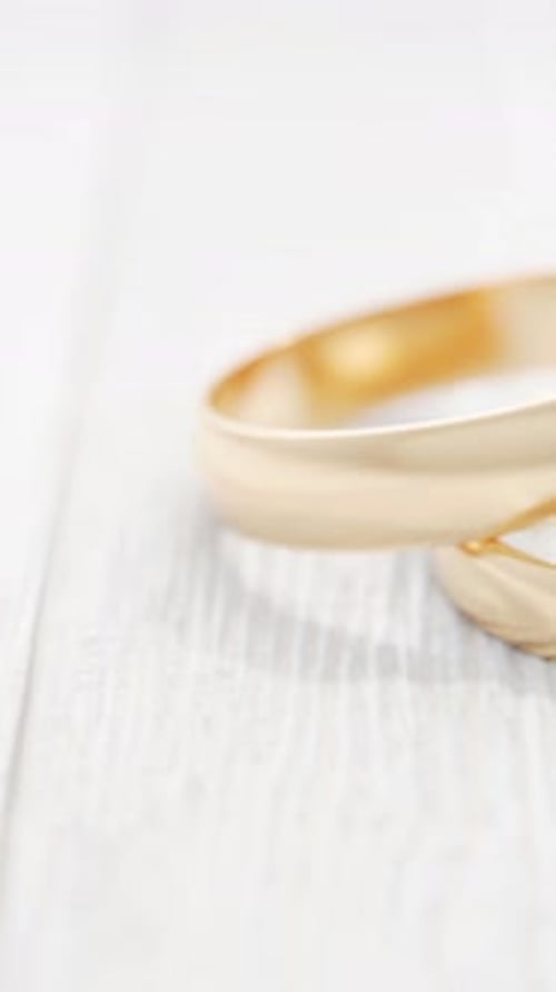 camera pans sideways past two gold wedding rings on a white wooden table.