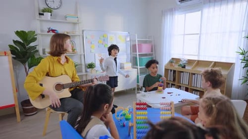Caucasian young woman teacher playing guitar with students in school.