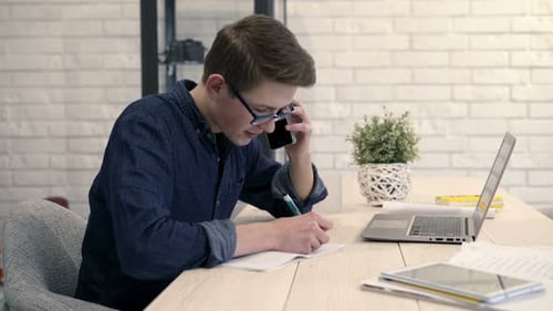 Jeune garçon se concentrant sur ses devoirs et parlant au téléphone portable à la maison