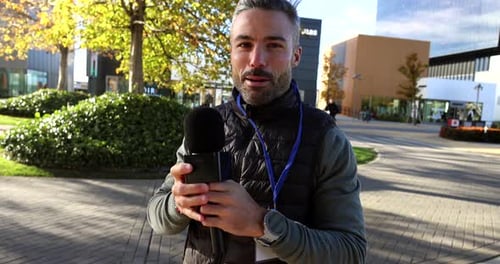 Professioneller männlicher Journalist mit Presseausweis, der ein Mikrofon in der Hand hält und mit der Kamera spricht, Repo