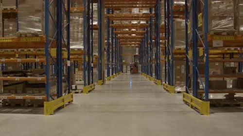 Un chariot élévateur à fourche fait demi-tour dans un long couloir d'un entrepôt logistique