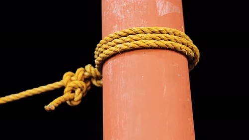 Vue rapprochée de la corde jaune enroulée autour d'un poteau orange sur fond sombre