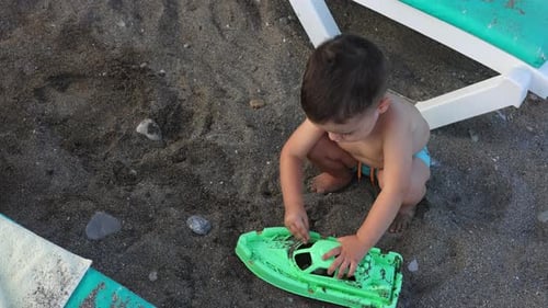 baby boy on beach playing with sheep boat toy.