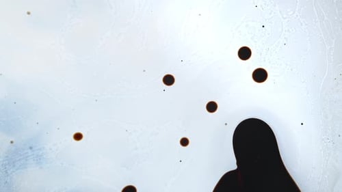 Brown liquid drops floating on a light background, abstract patterns forming in close-up shot