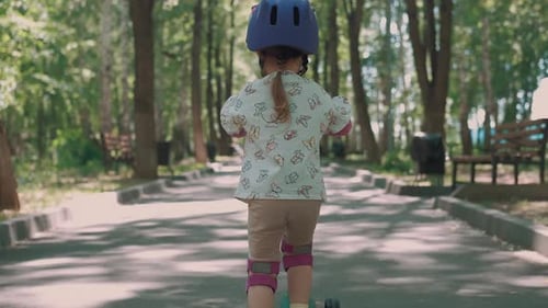Mom Teaches Daughter to Ride a Scooter in the Park in Summer