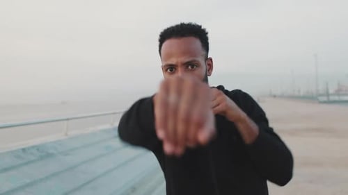 Young athlete boxer practicing punching technique while standing on the embankment