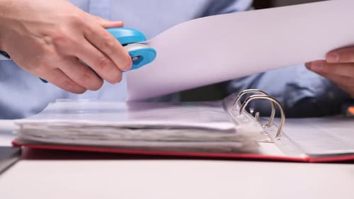 Office Worker Stapling Documents to a Folder Using a Blue Stapler