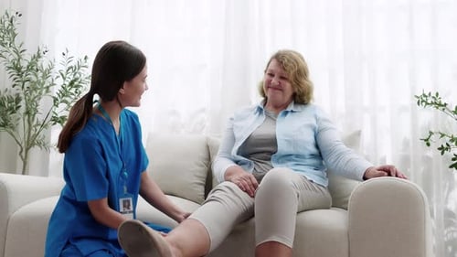 Young nurse physiotherapy with elderly patient while stretch leg in living room at home.
