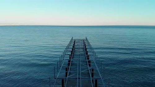 Die Kamera fliegt bei Sonnenuntergang über einen nicht funktionierenden Metallpier ohne Bodenbelag