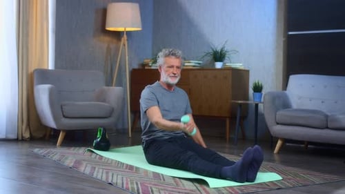 Senior Man Lifts Dumbbell on Yoga Mat Indoors