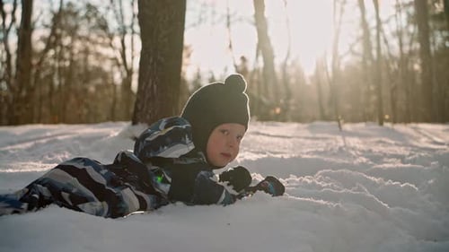 A cheerful child is happily lying around in a snowdrift in the forest.