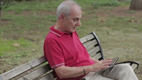 Friendly handsome old man with tablet computer in park