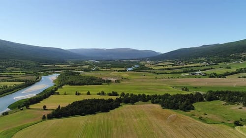 Aerial view of a serene river meandering through lush agricultural fields and distant mountains.