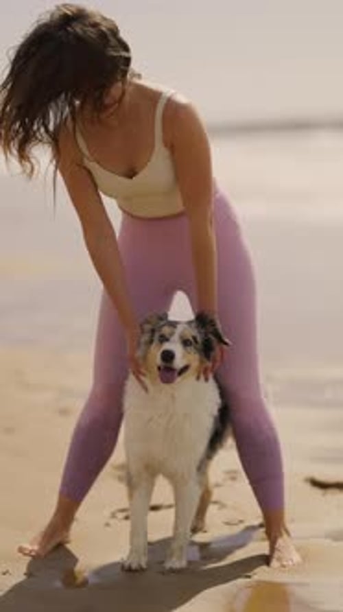 Young Woman in Sportswear Hugging Her Dog on a Sandy