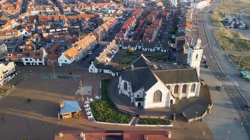 Aerial view of a coastal town with a historic white church, red-roofed houses, and nearby sand dunes